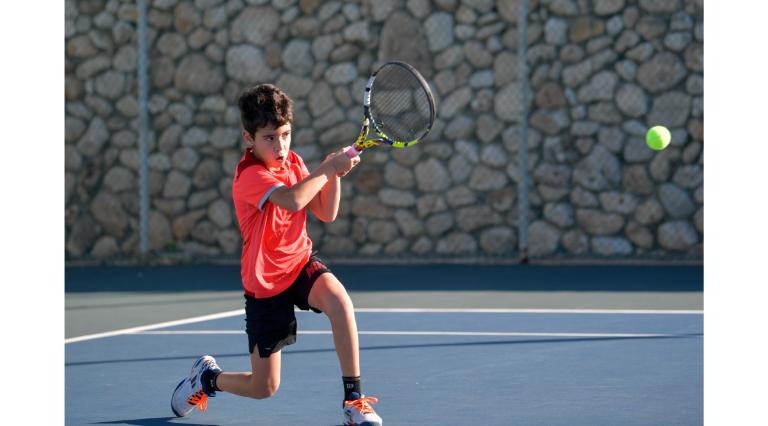 ילד חולצה כתומה חובט בכדור במגרש